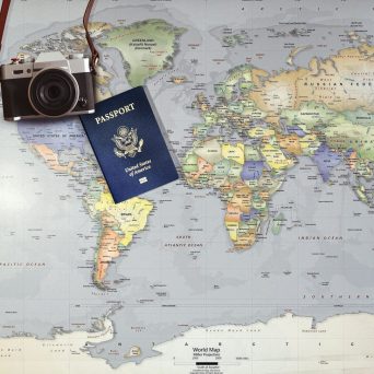 Passeport et appareil photo posés sur une carte du monde représentant les missions internationales de VILA’GENCIS